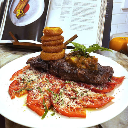 Appetizing plate of steak on top of a baked sliced tomato